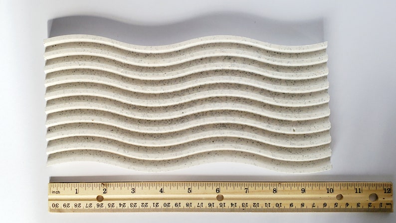 May include: A white, speckled, wavy silicone baking mat measuring 12 inches long. The mat has 10 raised, wavy lines.
