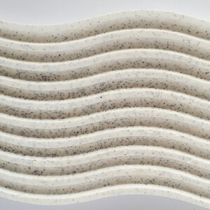 May include: A white, wavy, textured surface with a speckled pattern. The surface is made of a material that resembles concrete or plaster.
