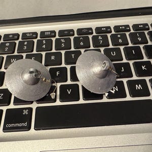 May include: Two silver-colored, disc-shaped earrings with a textured surface and a small loop for the ear wire. The earrings are resting on a black keyboard.