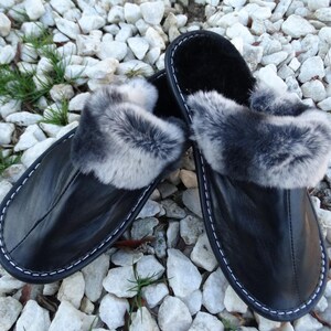 May include: Black leather slippers with a faux fur trim. The slippers have a white stitching detail around the edge.