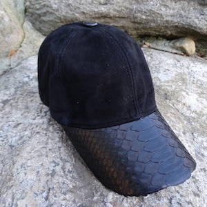 Può includere: Un berretto da baseball in pelle scamosciata nera con visiera in pelle di serpente nera.