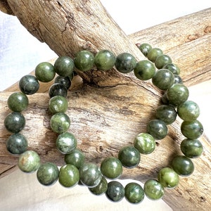 Puede incluir: Dos pulseras de cuentas de jade verde con un patr&oacute;n moteado verde y blanco. Las pulseras est&aacute;n apiladas una encima de la otra y descansan sobre un trozo de madera flotante.