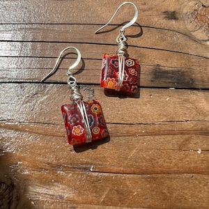 May include: A pair of silver wire wrapped earrings with red, orange and white floral patterned glass squares.