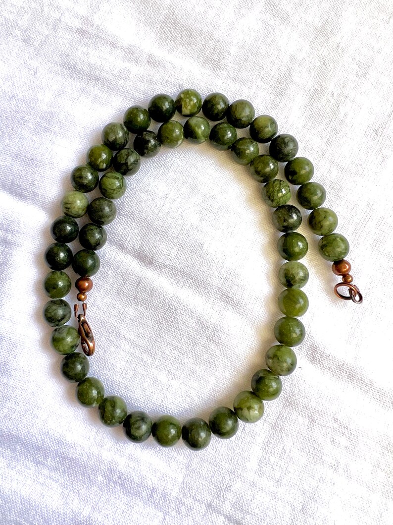 Puede incluir: Un collar de jade verde con cierres de cobre. El collar est&aacute; hecho de cuentas redondas y mide aproximadamente 45 cm de largo.