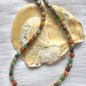 May include: A necklace made of orange and green gemstone beads with silver accents. The beads are square shaped and the necklace is displayed on a white surface.