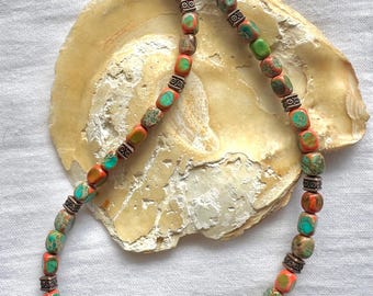 Puede incluir: Un collar hecho de cuentas de piedras preciosas de color naranja y verde con detalles plateados. Las cuentas son de forma cuadrada y el collar se muestra sobre una superficie blanca.