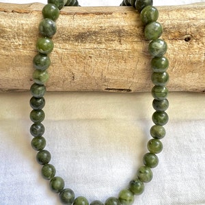 Puede incluir: Un collar de jade verde con cuentas redondas. El collar est&aacute; drapeado sobre un trozo de madera a la deriva.
