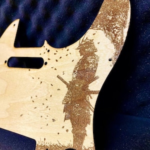 Puede incluir: Un golpeador de guitarra de madera de color claro con una imagen grabada con láser detallada de un guerrero samurái. El diseño incluye el guerrero, árboles y hojas que caen. El golpeador tiene agujeros pre-perforados para el montaje.
