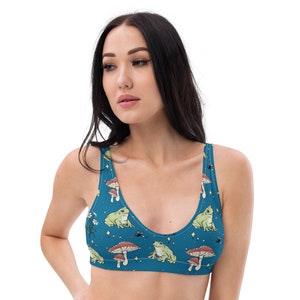 May include: A blue sports bra with a pattern of green frogs, mushrooms, and white flowers on a blue background.