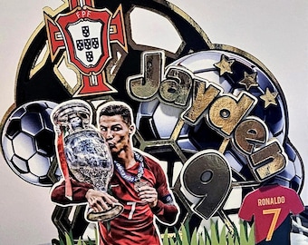 May include: A cake topper featuring a soccer theme with a soccer ball, a trophy, a soccer jersey, and the name "Jayden 9". The soccer jersey has the name "Ronaldo" and the number "7" on it. The trophy is a silver European Championship trophy. The soccer ball is black and white. The cake topper is decorated with gold accents.