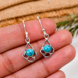 May include: A pair of silver dangle earrings with turquoise gemstones. The earrings have a delicate, intricate design.