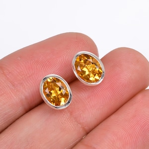 Może przedstawiać: Para srebrnych kolczyków z owalnymi, pomarańczowymi kamieniami z cytrynu.