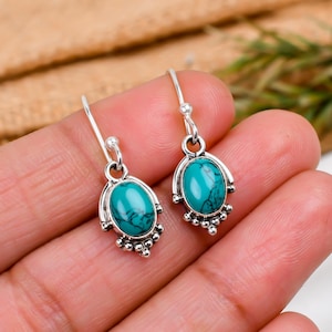 May include: A pair of silver dangle earrings with turquoise oval stones. The earrings have a delicate design with small beads around the stones.