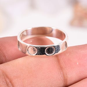 May include: A silver ring with a series of embossed circles around the band. The ring is shown close-up, highlighting the polished metal and the detailed circular patterns. The ring is a piece of jewelry.