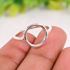 May include: A silver ring with a circular design. The ring features a smooth, polished finish and a minimalist aesthetic. The open circle is the focal point of the ring, creating a modern and elegant look. The ring is held by a person's fingers.