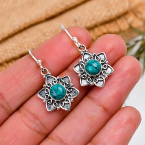 May include: Silver dangle earrings with a turquoise stone set in a floral design.