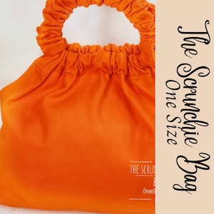 May include: Orange fabric bag with a gathered top and a single loop handle. The bag has the text "The Scrunchie Bag One Size" printed on the side.