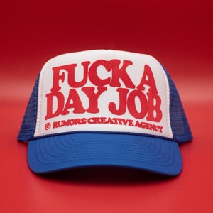 May include: A blue and white trucker hat featuring the red text "FUCK A DAY JOB". The hat has a mesh back and a curved peak. The text "RUMORS CREATIVE AGENCY" is printed below the main text.