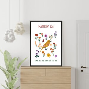 May include: A framed art print with a yellow bird illustration and floral elements. The text reads "Matthew 6:26" and "Look at the birds of the air". The print is displayed on a wooden chest of drawers. The print is in a black frame.