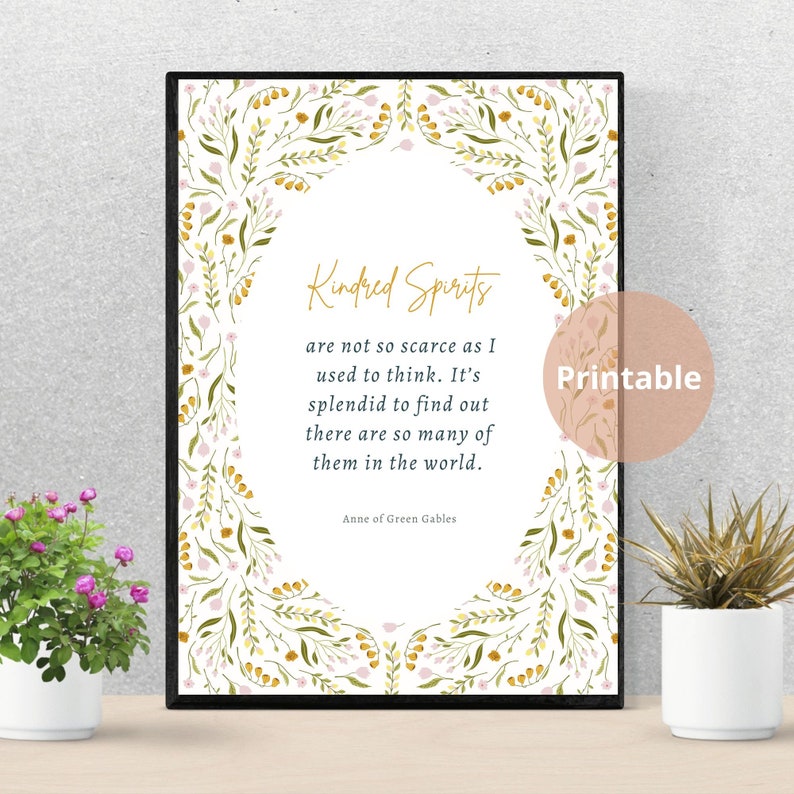 May include: A framed print with the quote "Kindred Spirits" in gold script, surrounded by a floral border. The quote is from Anne of Green Gables. A small, round "Printable" sticker is in the corner.
