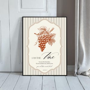 May include: Framed art print featuring a sepia-toned illustration of grapes and leaves. The text "I AM THE Vine" is displayed with a quote from John 15:5. The background has a beige and white striped pattern.