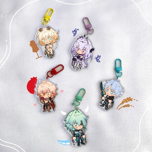 May include: A collection of five acrylic charm keychains featuring anime-style characters. Each charm has a different character design with vibrant colors and attached to a colored clasp. The characters have unique outfits and hairstyles.