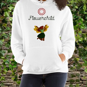 Op de afbeelding: Witte hoodie met een flower child-afbeelding en een rood bloemendesign. De afbeelding toont een vrouw met bruin haar en vleugels, die een groene rok en een wit shirt draagt.