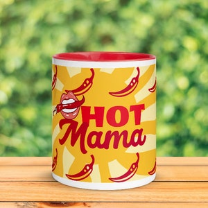 May include: A ceramic mug with a red interior and a white exterior. The mug features a yellow background with red chili peppers and the words "HOT Mama" in red script. A cartoon mouth with a chili pepper is also on the mug.