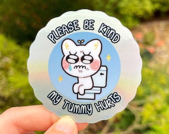 Puede incluir: Una pegatina blanca con fondo azul y un gato de dibujos animados sentado en un inodoro. El texto de la pegatina dice "Por favor, sé amable, me duele la barriga."