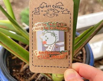 May include: A gold enamel pin with a cartoon illustration of a white animal with a red nose. The animal is in a bathroom stall with the text "WHY THE FOCK IS IT CALLED THE RESTROOM?" and "I AM FIGHTING FOR MY LIFE IN HERE!"