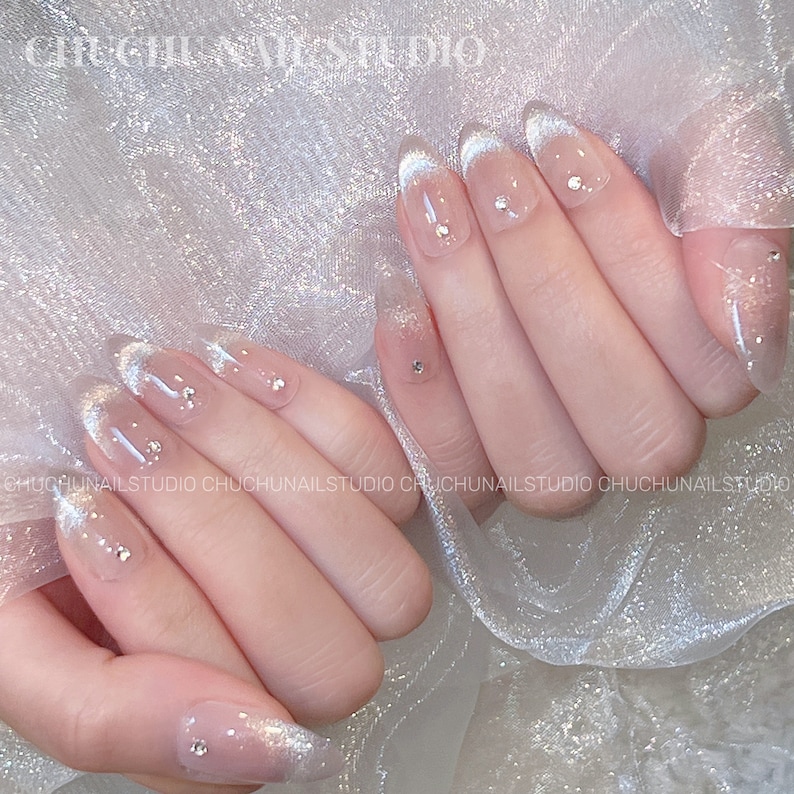 May include: A set of clear, oval-shaped, press-on nails with a white tip. The nails have small, clear rhinestones on top.