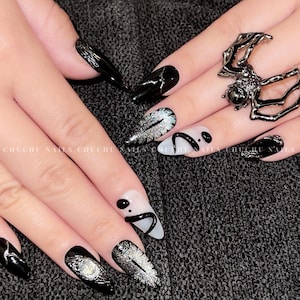 Peut inclure: Art de l'ongle noir et blanc avec une bague araignée. Les ongles sont longs et pointus, avec une variété de motifs, y compris des paillettes, des tourbillons noirs et blancs et une toile d'araignée noire.