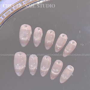May include: Ten pink and white oval-shaped false nails with silver glitter and rhinestones. The nails are arranged in two rows on a reflective surface. The text 'CHUCHUNAIL STUDIO' appears at the top of the image.