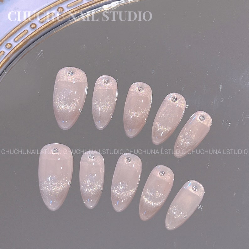 May include: Ten pink and white oval-shaped false nails with silver glitter and rhinestones. The nails are arranged in two rows on a reflective surface. The text 'CHUCHUNAIL STUDIO' appears at the top of the image.
