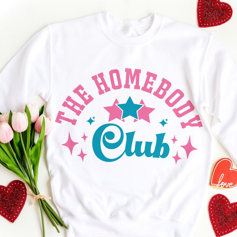May include: White sweatshirt with a pink and blue graphic design that says "The Homebody Club" with stars and sparkles.
