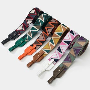 Puede incluir: Una colección de correas de bolso estampadas con un diseño en zigzag. Las correas muestran una variedad de colores, incluyendo rojo, verde, naranja, amarillo, rosa y morado. Los extremos son de cuero y tienen herrajes metálicos.