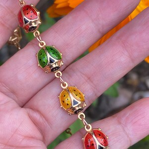 May include: A gold chain bracelet with five enamel ladybug charms. The ladybugs are red, yellow, and green with black spots.