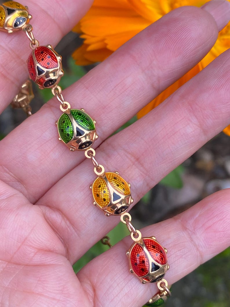 May include: A gold chain bracelet with five enamel ladybug charms. The ladybugs are red, yellow, and green with black spots.