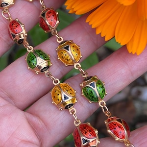 May include: A gold chain bracelet with a series of ladybug charms. The ladybugs are enameled in red, green, and yellow with black spots.
