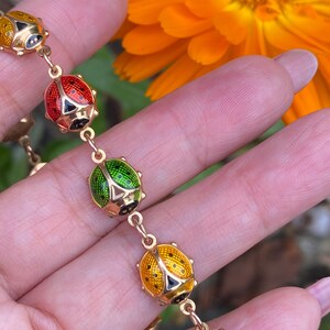 May include: A gold chain bracelet with five ladybug charms. The ladybugs are enameled in red, green, and yellow with black spots.