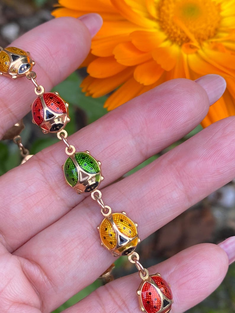 May include: A gold chain bracelet with five ladybug charms. The ladybugs are enameled in red, green, and yellow with black spots.