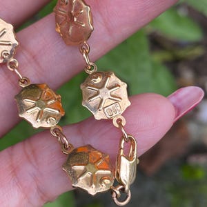 May include: A gold chain bracelet with a clasp and a series of oval links. Each link features a raised starburst design.