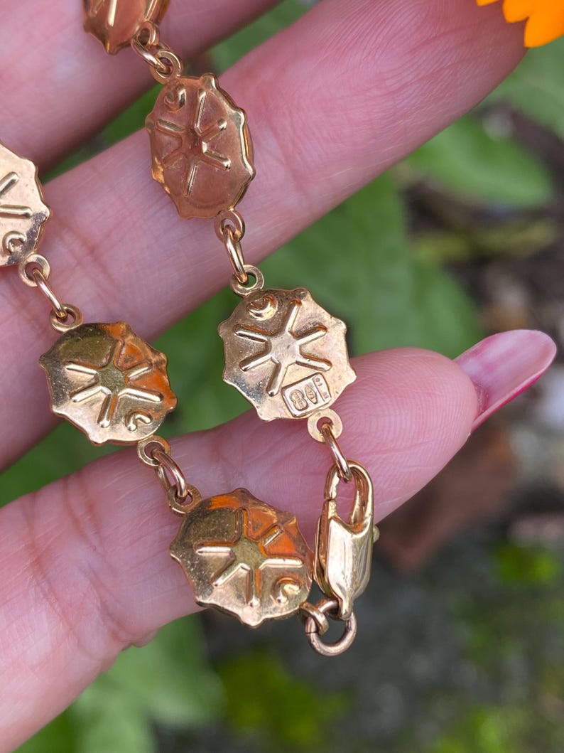 May include: A gold chain bracelet with a clasp and a series of oval links. Each link features a raised starburst design.