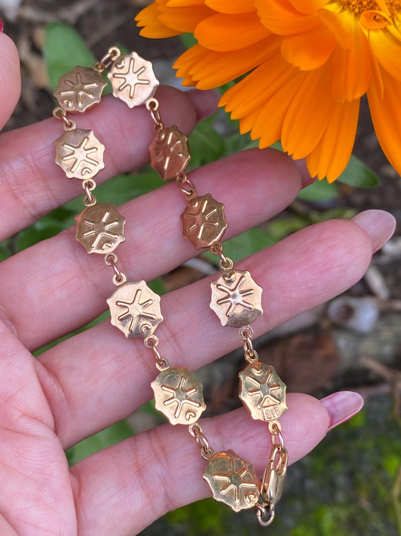 May include: Gold bracelet with a chain and round charms featuring a starburst design.
