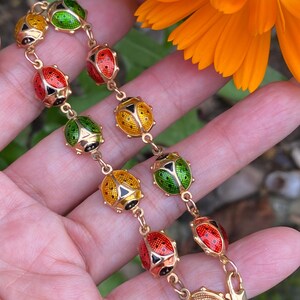 May include: A gold bracelet with a chain of small, round, enamel ladybug charms. The ladybugs are red, yellow, and green with black spots.
