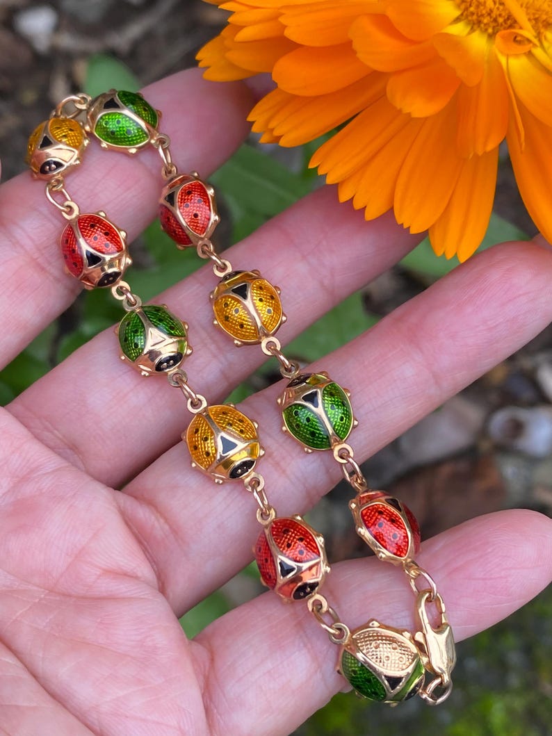 May include: A gold bracelet with a chain of small, round, enamel ladybug charms. The ladybugs are red, yellow, and green with black spots.