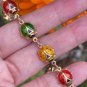 May include: A gold chain bracelet with four ladybug charms. The ladybugs are red, green, yellow, and red with black spots.