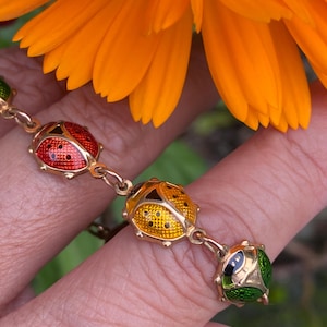 May include: A gold chain bracelet with four enamel ladybug charms. The ladybugs are red, yellow, green, and black.