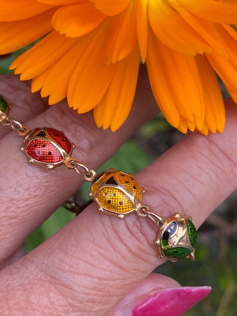 May include: A gold chain bracelet with four enamel ladybug charms. The ladybugs are red, yellow, green, and black.
