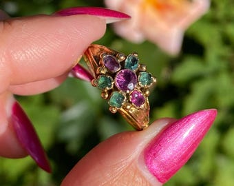 May include: A gold ring with a cluster of pink and green gemstones. The ring is set with a central pink stone surrounded by smaller green stones.